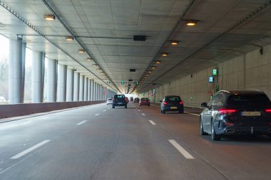 Araçlar gündüz vakti beton duvarları olan iyi aydınlatılmış bir yeraltı tüneli boyunca sürüyorlar. Trafiğe yeşil yön işaretleri rehberlik eder, pürüzsüz navigasyon sağlar.