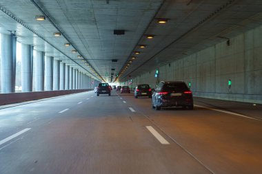 Beton sütunlar ve parlak ışıkların yer aldığı geniş bir otoyol tünelinde birkaç araba geziniyor. Atmosfer sakin ve düzenli. Bu da yoğun ama verimli bir trafik akışını gösteriyor..