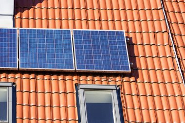 Gündüz vakti berrak mavi gökyüzünün altında yenilenebilir enerji üretmek için güneş ışığını yakalayan güneş panelleri modern bir evin teras çatısına monte edilir..