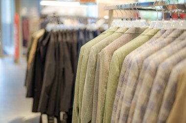 Modern bir giyim mağazasındaki askılarda moda ceketlerden oluşan bir koleksiyon sergileniyor. Kurulumda çeşitli dokular ve sessiz renkler yer alıyor, müşterileri gezmeye davet ediyor.