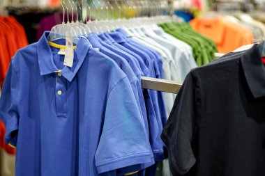 Parlak renkli polo gömlekler canlı bir perakende mağazasındaki askılarda düzgün bir şekilde düzenlenir. Müşteriler çeşitli seçenekleri inceleyerek moda seçeneklerini keşfediyorlar..