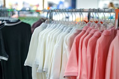 Yoğun bir perakende mağazasında polo gömleklerinin farklı tonları düzgünce sergileniyor. Alışverişçiler çevreyi kolaçan ederek, günlük moda tercihleri için canlı bir atmosfer yaratıyorlar..