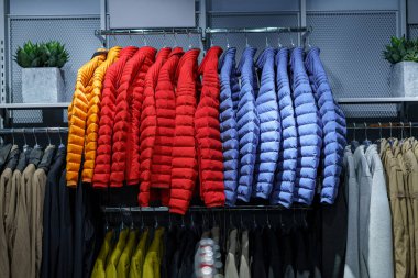 Parlak renkli ceketler modern bir giyim mağazasının rafında güzelce asılı. Alışverişçiler, sonbahar havası geldiğinde, daha serin günler için şık seçenekler arayarak seçime göz atıyorlar..