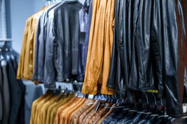 Bir perakende mağazasında çeşitli deri ceketler raflarda asılı, farklı renkler ve dokular sergileniyor. Sıcak tonlar davetkar bir atmosferdeki serin gölgelerle tezat oluşturuyor..