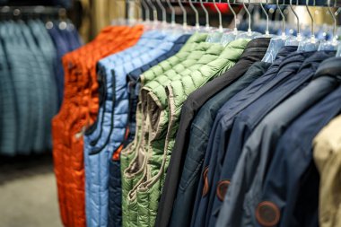 Bir perakende mağazasındaki askılara çeşitli renkli ceketler asılıdır. Düzenleme farklı stil ve renkler sergiliyor, müşterileri sonbahar moda seçimlerini keşfetmeye davet ediyor.