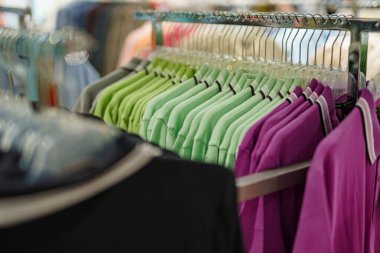 Bir perakende mağazasında çeşitli parlak renkli polo gömlekler sergileniyor. Bu bölümde yoğun, iyi organize edilmiş bir rafta yeşil ve mor renkli renkler var..