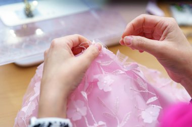 Eller, doğal ışık ve yaratıcı enerjiyle dolu rahat bir dikiş atölyesinde çiçeklerle süslenmiş karmaşık pembe kumaşı ustalıkla birleştirir..