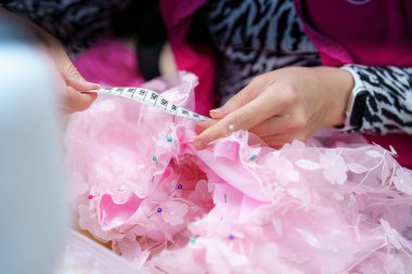 Yetenekli bir işçi canlı bir dikiş atölyesinde çiçeklerle süslenmiş yumuşak pembe kumaşı ölçmeye odaklanır. Güzel bir elbise yaratmak için kusursuz bir iş çıkarılıyor..