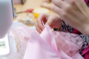 Pembe kumaşı ustalıkla dikebilen bir insan, öğleden sonraları atölye ortamında karmaşık detaylara odaklanır. Araçlar ve malzemeler görünür, yaratıcı bir atmosfer yaratıyor..