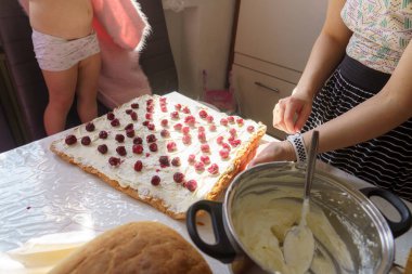 Arkadaşlar parlak bir mutfakta taze böğürtlenli büyük bir pasta hazırlıyorlar. Bir kişi dekorasyonla meşgulken diğeri de yakınlarda hazırlanıp şenlik atmosferinin tadını çıkarıyor..