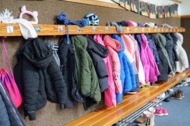 Okul koridorundaki ahşap bir askıda çeşitli renklerde bir dizi canlı kışlık ceket sergileniyor. Dekorun, yukarıdaki kişisel aksesuarlarla vurgulanmış rahat bir atmosferi var..