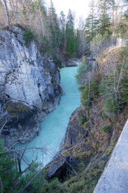 Turkuaz bir nehir, yemyeşil ağaçlarla çevrili kayalık bir kanyon boyunca kıvrılır. Huzurlu sahne, ormanlık alandaki doğanın güzelliğini vurgular..