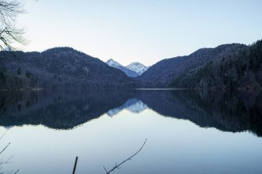 Sakin bir göl, yüksek dağların arasında sessizce oturur, tepeleri karla kaplanır. Sakin su, sakin manzarayı mükemmel bir şekilde yansıtıyor. Şafak vakti çarpıcı bir manzara yaratıyor..