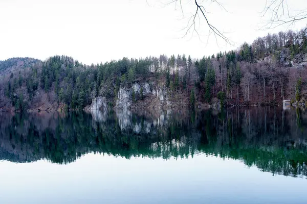 Sabahın erken saatlerinde sakin bir göl üzerinde dingin bir parıltı sarıyor. Yoğun ormanlar ve engebeli uçurumlar ortaya çıkıyor. Durgun su manzarayı çok güzel yansıtıyor. Huzurlu bir atmosfer yaratıyor..