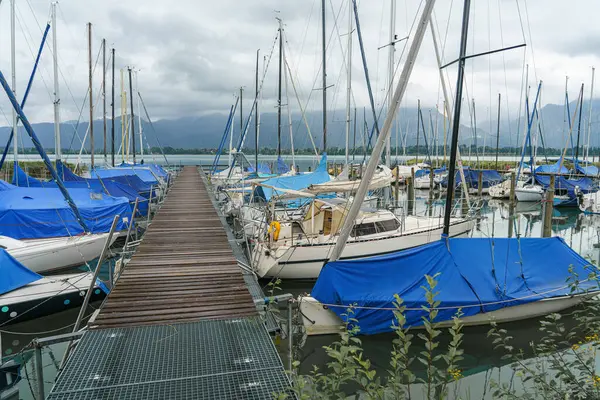 Huzurlu bir marinada, mavi brandalarla kaplı çok sayıda yelkenli iskeleye yanaşır. Çevresi uzak dağlarla çevrili ve gökyüzü bulutlu. Bu da soğuk havayı gösteriyor..