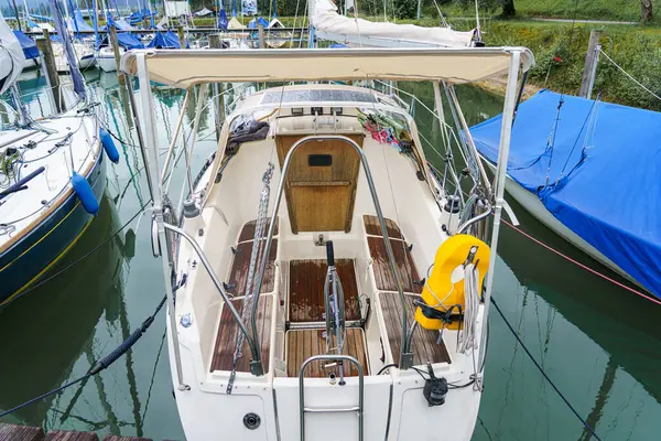 Bir yelkenli, sakin bir marinaya yanaşır. Ahşap güvertesi, sakin atmosferi yansıtır. Yakınlarda tekneler demirler ve sakin sular güneşli bir günde huzurlu bir manzara yaratır..