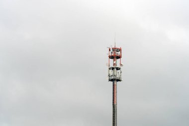 Antenleri olan yüksek bir iletişim kulesi şehrin üzerinde yükseliyor, gri bulutlarla çevrili. Bu yapı kablosuz iletişim ve sinyaller için çok önemli..