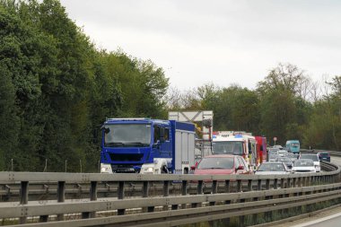 Kamyonlar ve arabalar da dahil olmak üzere otoyolda araçlar durdurulurken, yardım için bulutlu gökyüzünün ortasında acil durum araçları yol alıyor.