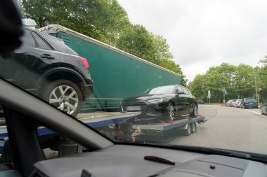 Bulutlu bir öğleden sonra, bir nakliye kamyonunun teslimat için birkaç araba yüklediği görüldü. Kentsel bir ortamda otomotiv lojistiği sürecini gösteren iki araç görünür..