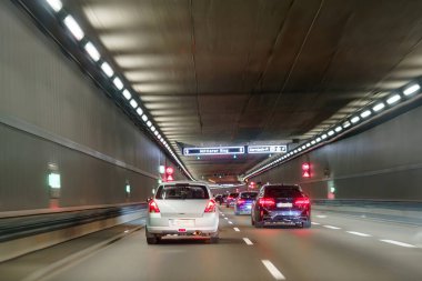 Araçlar, gece erken saatlerde yön işaretleriyle işaretlenmiş iyi aydınlatılmış bir tünelden geçiyor. Tasarım düz duvarlar ve aydınlık şeritler içeriyor, güvenli bir sürüş atmosferi yaratıyor..