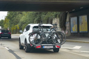 Beyaz bir SUV bisiklet parkında iki bisiklet taşıyan bir şehir caddesinde geziniyor..