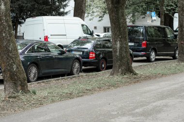 Lüks arabalar ağaçlarla kaplı sakin bir şehir caddesi boyunca park halindedir. Sahne, gün boyunca bakımlı araçlar ve yeşilliklerle sakin bir ortam yakalıyor..