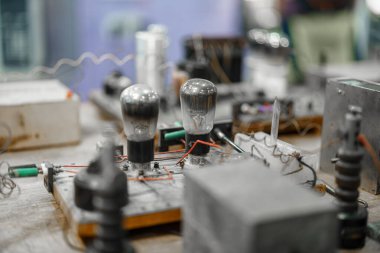 Bir atölye ortamında antika elektronik parçaların görüntüsü. Vintage ampuller ve kablolama teknolojinin evrimini gösteriyor. Atmosfer nostaljik ve eğitici..