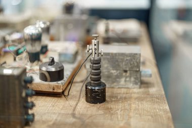 Çeşitli antika elektrikli ekipmanlar bir atölyedeki ahşap bir masanın üzerine düzgünce dizilir. Ögeler arasında eski bir döneme ait kablolar, anahtarlar ve vakum tüpleri yer alıyor..