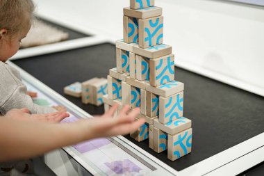 Genç bir çocuk çağdaş bir öğrenme ortamında renkli blokları istiflemeye konsantre olur. Bloklardaki canlı tasarımlar inşa etme deneyimini güçlendiriyor..