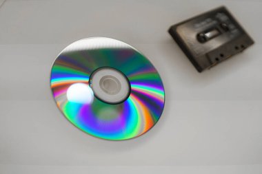 Canlı bir CD, temiz beyaz bir yüzey üzerinde klasik bir kasetin yanında duruyor..