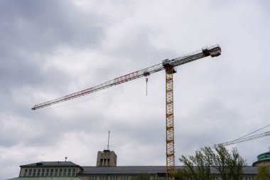 Büyük bir inşaat vinci bulutlu bir gökyüzüne karşı, kentsel alandaki bir inşaat projesinin bir sonraki aşaması için hazırlanıyor. Atmosfer yaklaşan yağmurla ağırlaştı..