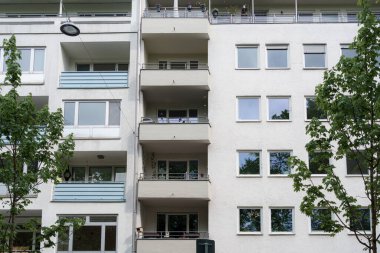 Çağdaş bir apartmanın birden fazla balkonları görülebilir, ağaçlar ve güneş ışığıyla çevrili..