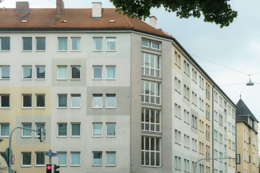 Çağdaş bir apartman binasında, gökyüzü bulutlu ve sokak işaretlerini yansıtan pencereler ve konut alanlarında çeşitli renkler ve tasarımlar sergilenmektedir..