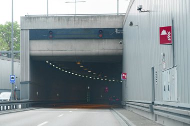 Araçlar kırmızı sinyallerin durması gerektiğini gösterdiği tünel girişine yaklaşır. Modern yapıda sürücüler için silindirik bir tasarım ve açık tabela bulunmaktadır..