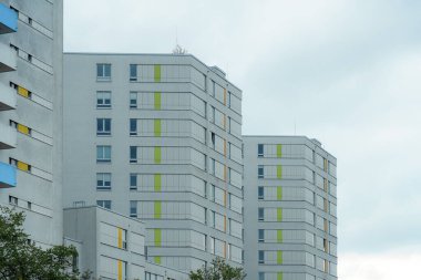 Beyaz ve renkli aksanların bir karışımını sergileyen modern apartman manzarası. Yapılar bulutlu bir gökyüzünün ortasında yükseliyor, kentsel bir ortamda çağdaş mimariyi sergiliyor..