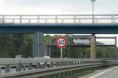 Saatte 60 km hızla giden bir otoyolun net bir görüntüsü var. Yeşillik yol kenarındayken, bir üstgeçit üstümüzden geçiyor. Hava bulutlu görünüyor..