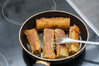 Kızarmış börekler ocağın üstünde siyah bir tavada cızırdıyor. Çatal, gevrekliklerini kontrol etmek için kullanılır. Öğlen oldu ve mutfakta davetkar bir atmosfer var..