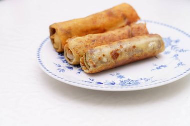 Üç tane altın sarısı börek bir çiçek tabağına yerleştirilmiş ve çıtır çıtır dokularını sergiliyorlar. Mutfak ışığı, nefis atıştırmalıkları ön plana çıkararak sahneyi aydınlatıyor..