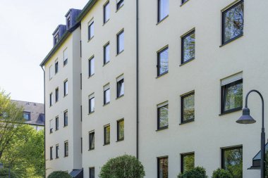 Modern bir konut binasında yeşilliklerle çevrili büyük pencereler bulunur. Yapı basit çizgiler ve yeterli ışık ile tasarlanmıştır. Burası huzurlu bir şehir ortamı..