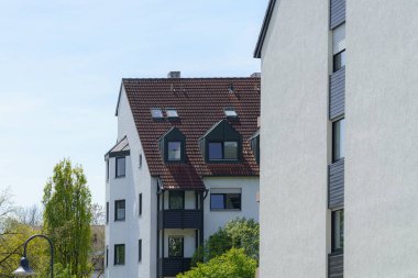 Parlak güneş ışığı, kentsel bir mahallede yemyeşil ortamda kurulmuş çağdaş konut binalarını aydınlatır. Mimaride değişik pencere stilleri ve hoş bir ortam vardır..