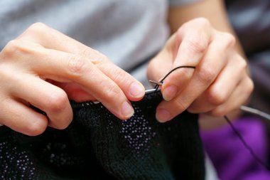 Bir insan iplik ve iğneleri manipüle etmek için iki elini kullanarak örgü örmeye odaklanır. Mekan rahat ve davetkar. Evde verimli bir öğleden sonranın özünü yakalıyor..