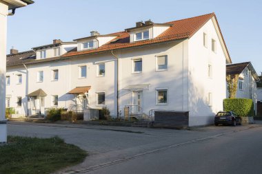 Huzurlu bir cadde boyunca yan yana duran iki beyaz bina. Öğleden sonranın ılık ışığı onların temiz çizgilerini ve basit mimarisini vurguluyor ve sakin bir atmosfer yaratıyor..