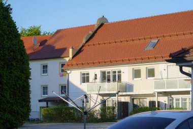 Kırmızı kiremit çatılı banliyö evleri görünür, gösterişli balkonlar ve yeşil alanlar. Akşam ışığı, mimari özellikleri ve yakınlardaki çamaşır iplerini vurguluyor..