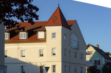 Sivri uçlu çatısı olan güzel işçilikli bir bina sıcak akşam güneşiyle aydınlatılır. Mimari büyüleyici detaylar sergiliyor ve sakin çevreyle çelişiyor..