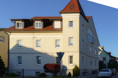 Modern bir konut binası, sakin akşam ışığı sırasında yemyeşil ve diğer yerleşim yapılarıyla çevrili klasik özellikleriyle zarif bir şekilde duruyor..