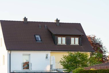 Çağdaş bir evde eğimli bir çatı ve sessiz bir alanda yer alan büyük pencereler bulunur. Bereketli yeşillik, açık mavi gökyüzünün altındaki cazibesini artırıyor..