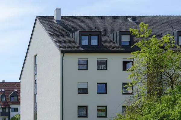 Sakin bir yerleşim bölgesinde birden fazla penceresi olan modern bir bina bulunur. Yeşillik, yapıyı çevreleyerek huzurlu bir ortam yaratır. Parlak gün ışığı tüm cazibeyi arttırır.