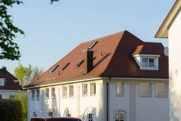 Parlak güneş ışığı, eğimli çatısı ve tavan penceresi olan büyüleyici bir konut binasını aydınlatıyor. Gün boyunca berrak mavi gökyüzü altında sakin bir semti gözler önüne seriyor..