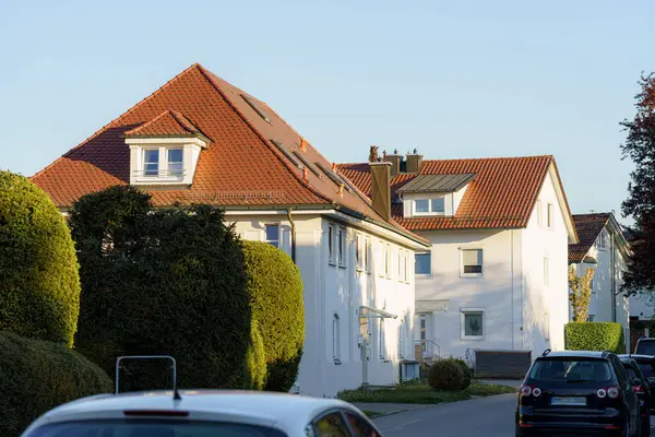 Sakin bir banliyö sokağı öğleden sonra güneşinin sıcacık parıltısıyla yıkanır, bakımlı evler ve yolu kaplayan çitlerle..