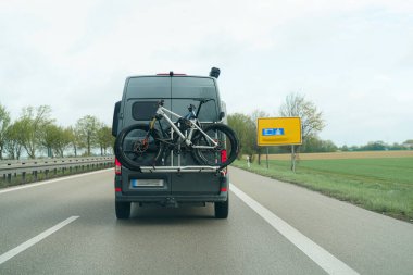 Gri bir minibüs, manzaralı bir otoyolda giderken bisiklet parkında iki dağ bisikleti taşıyor. Yol yemyeşil yemyeşil, önümüzde barışçıl bir açık hava macerası var..